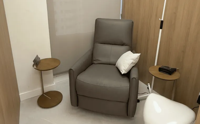 Poltrona reclinável de couro cinza com almofada, mesa de apoio redonda e suporte de soro, em cabine de madeira clara