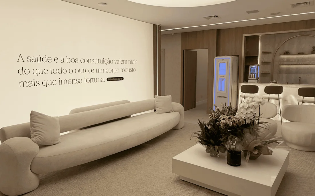 Recepção do Instituto Evollution: sofás claros em volta de uma mesa de centro com flores, e frase da marca na parede
