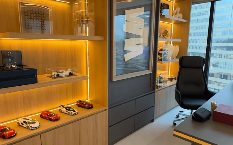 Sala do Dr. Sandro Ferraz no Instituto Evollution: prateleiras iluminadas com miniaturas de carros, poltrona de couro e mesa de trabalho junto à janela